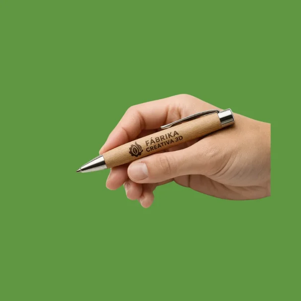 Bolígrafos madera Eco Mano sosteniendo un bolígrafo de madera sobre un fondo verde.